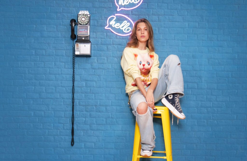 Schönes Mädchen im Selfie-Studio vor einer blauen Ziegelwand mit Münztelefon