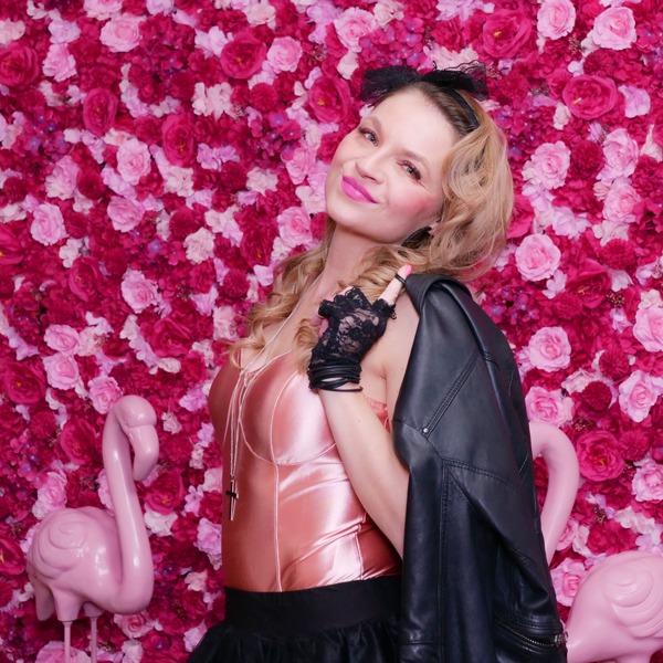 Schöne junge Frau im Selfie Studio vor einer Blumenwand mit rosa Flamingos
